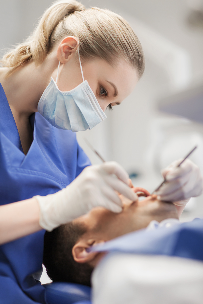 people, medicine, stomatology and health care concept - female dentist with dental mirror and probe checking up male patient teeth at dental clinic office